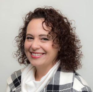Smiling woman with curly hair, plaid attire.