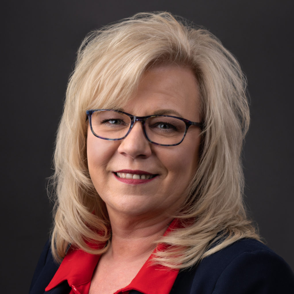 Blonde woman with glasses smiling warmly.