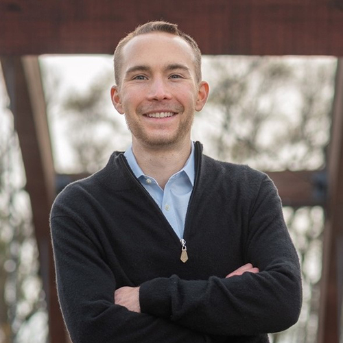 Smiling man outdoors with crossed arms.