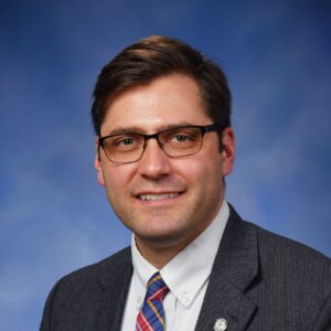 Man in suit with glasses smiling.