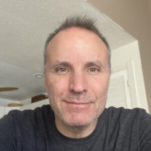 Man smiling in a room with white walls.