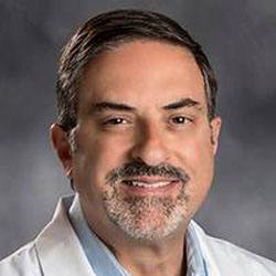 Smiling man in white coat, gray background.