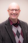 Smiling man in a suit and sweater.